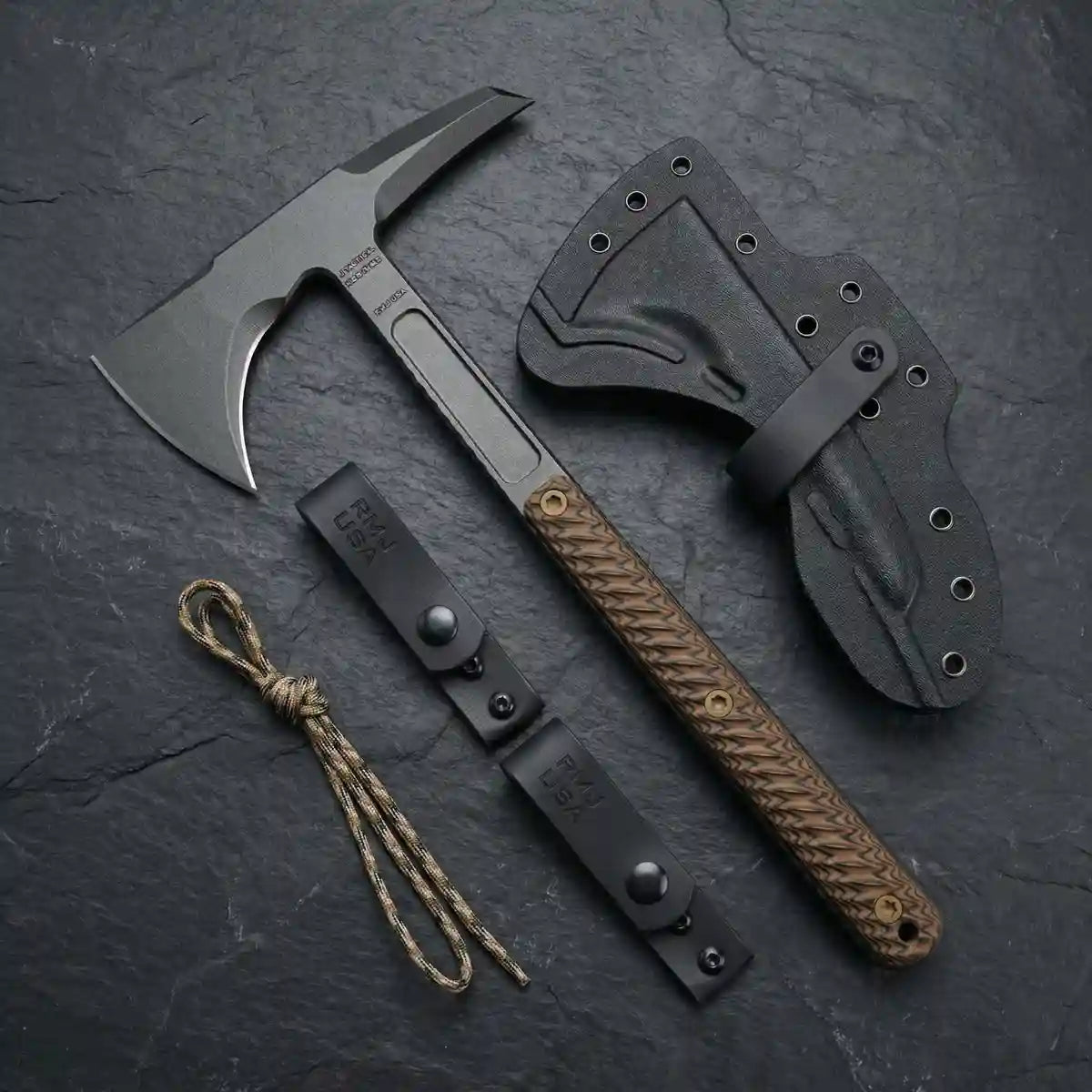 Premium tactical tomahawk axe with a textured G10 handle, shown flat-lay on a black slate background alongside its custom black kydex sheath, RMJ USA belt loops, and camo paracord lanyard.