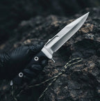 A tactical Bowie knife with a 14-inch D2 steel clip-point blade held in a gloved hand, showcasing its robust design and handle ergonomics against a dark stone background.