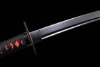 Close-up of a sleek black katana blade and collar habaki, featuring a black wrapped hilt over red ray skin and a minimalist black square tsuba handguard against a dark backdrop.