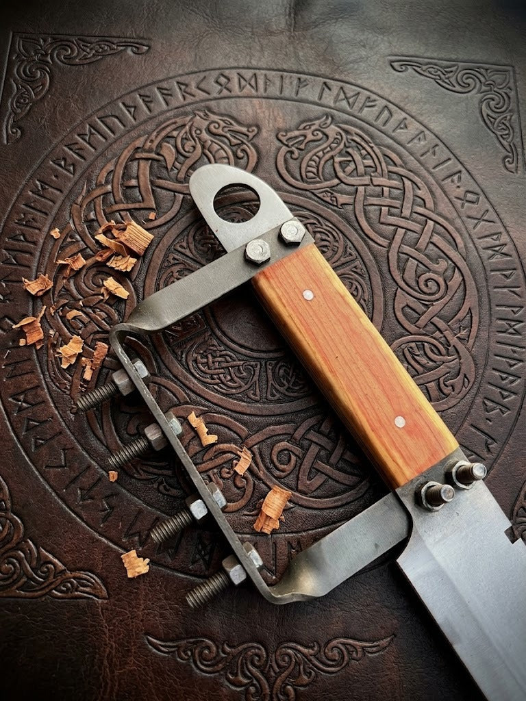 A close-up of a custom tactical dagger handle featuring unique bolt-reinforced steel guards and an ergonomic wood grip, resting on an intricate leather mat with engraved Norse rune patterns.