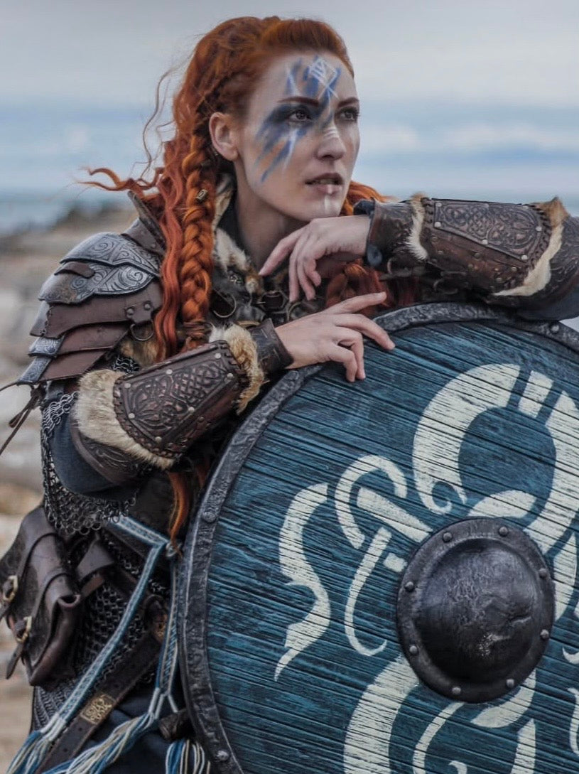 Viking warrior with traditional face paint, wearing detailed leather gauntlets and armor, leaning on a handcrafted wooden dragon shield.