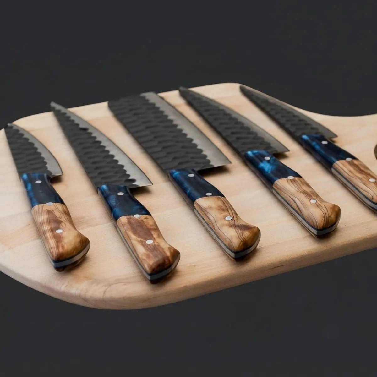 A premium 5-piece kitchen knife set with hammered finish blades and unique blue resin and wood handles, arranged on a wooden board.