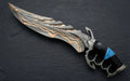 A professional studio shot of a handmade Damascus steel fantasy medieval dagger with a dark skeleton knuckle-duster handle and vibrant turquoise stone inlay resting on a dark slate surface