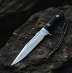 A professional handmade tactical Bowie knife featuring a 14-inch D2 steel clip-point blade and black Micarta handle with a paracord lanyard, displayed on a dark rocky surface