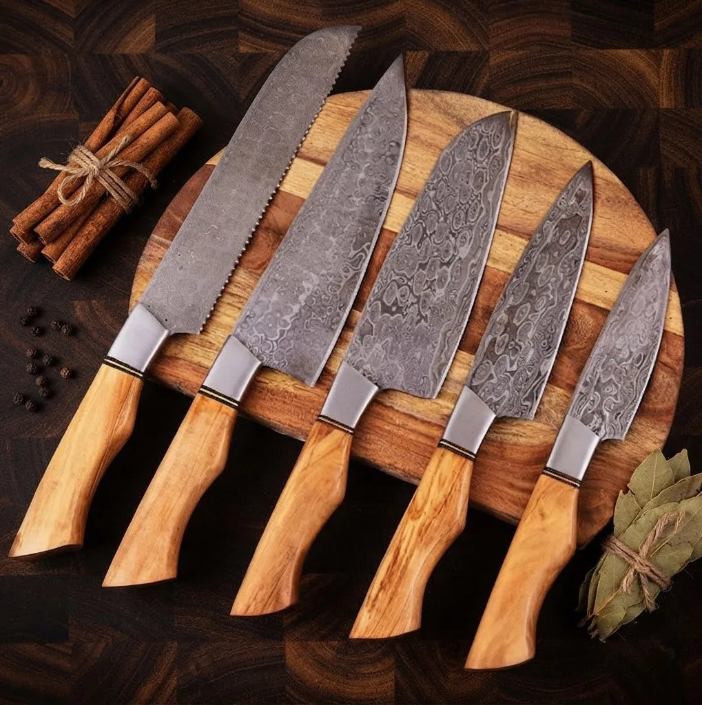 A professional set of hand-forged Damascus steel kitchen knives featuring natural olive wood handles, arranged on a round wooden cutting board with cinnamon sticks and bay leaves.