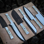 A collection of premium hand-forged kitchen knives featuring unique marble-effect resin handles, showcased with their custom-fit protective leather sheaths on a rustic background.
