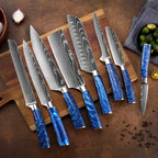 High-contrast Damascus steel kitchen knives with vibrant blue resin handles arranged on a wooden cutting board with fresh limes and onions on a textured rustic background.