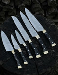 A premium 6-piece handcrafted kitchen knife set with sleek black handles and brass bolsters, arranged beautifully on a dark rustic wooden tree stump background.