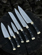 A premium 6-piece handcrafted kitchen knife set with sleek black handles and brass bolsters, arranged beautifully on a dark rustic wooden tree stump background.