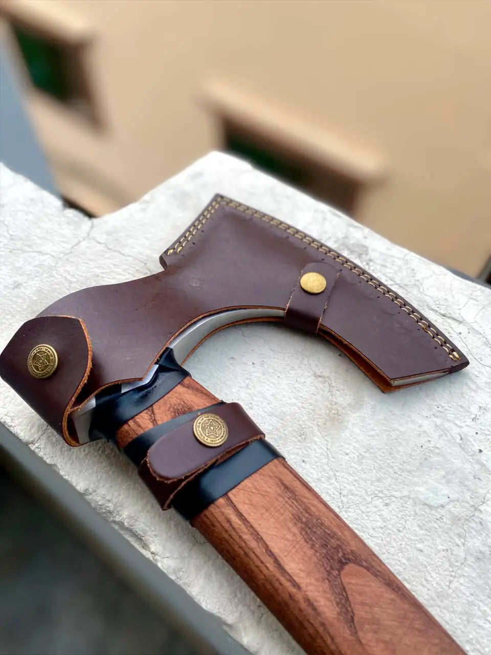 Detail view of a custom protective leather mask and belt loop strap for a hand-forged Norse hatchet, showcasing heavy-duty leather craftsmanship and secure brass fasteners for outdoor utility.