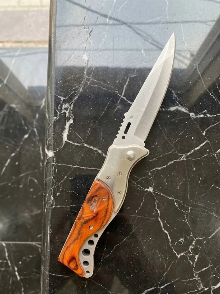 Premium custom EDC folding knife displayed open to show blade mechanics and full body profile, featuring durable stainless steel construction and a unique burls wood grip handle accent on a luxury stone background.
