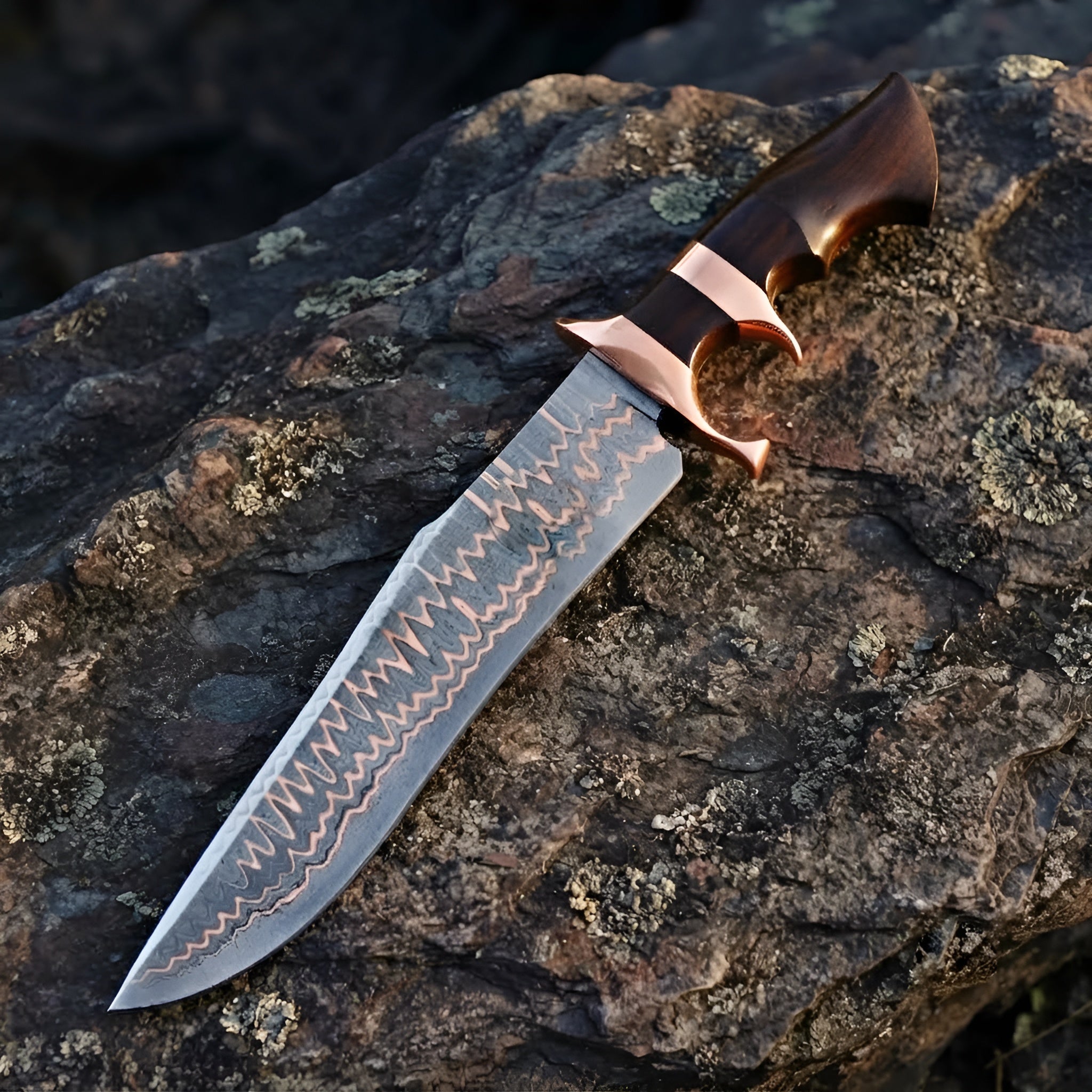 Close-up of a handmade Copper Damascus Bowie knife, showcasing the unique copper-layered steel pattern, double copper guard, and rich wood handle on a stone background