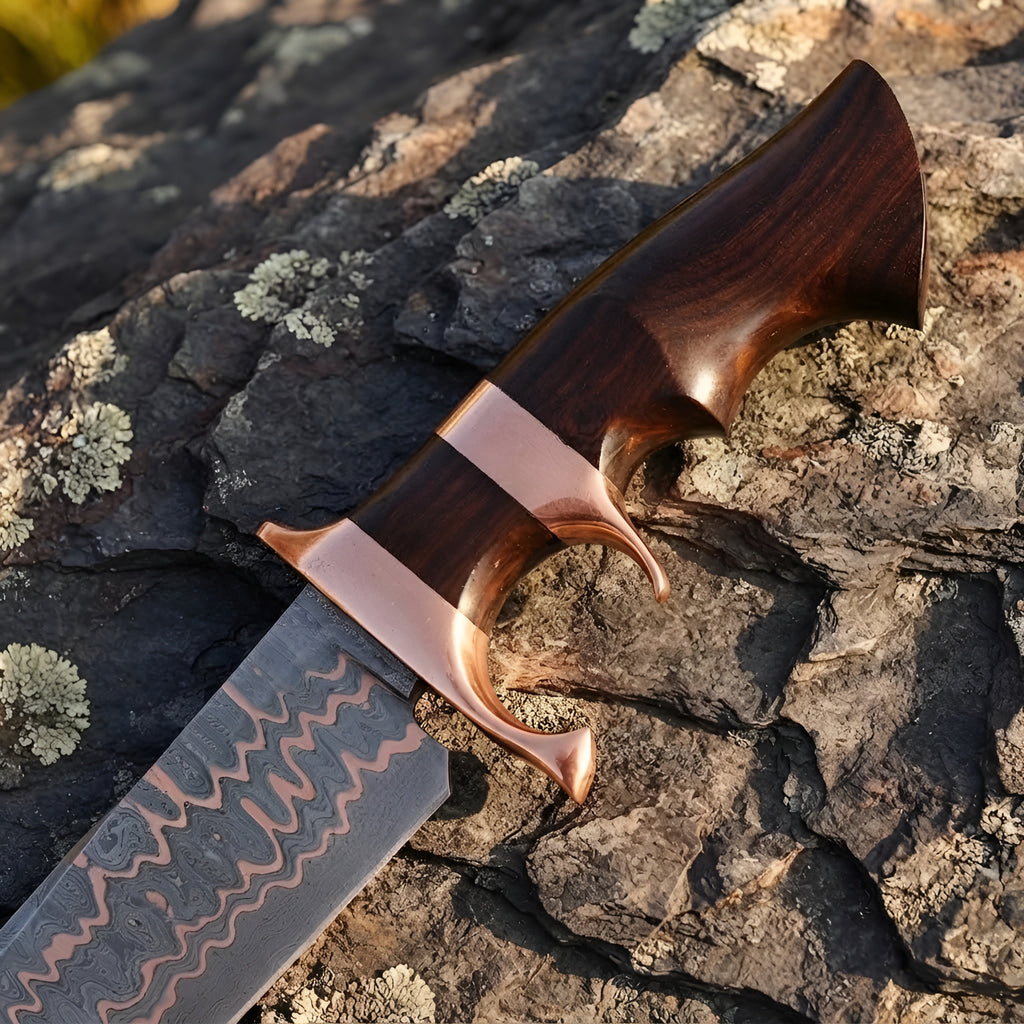 Close-up of a handmade Copper Damascus Bowie knife, showcasing the intricate double copper guard, ergonomic wood handle, and copper-layered blade on a textured stone background