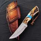 A professional handmade D2 steel cowboy knife featuring a 5mm blade with rasp texture, stag antler handle with turquoise inlay, and leather lanyard, displayed next to its matching tool-stamped leather sheath on a dark stone background