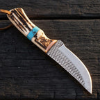 A professional handmade D2 steel cowboy knife featuring a 5mm blade with a diamond rasp pattern, copper bolster, and stag antler handle with a vibrant turquoise inlay on a dark wooden background.