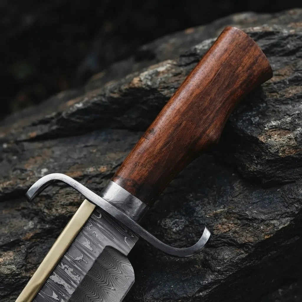 Close-up of a handmade Damascus Bowie knife, showcasing the rich-grained Rosewood handle, solid metal bolster, and intricate wavy Damascus steel pattern on the blade