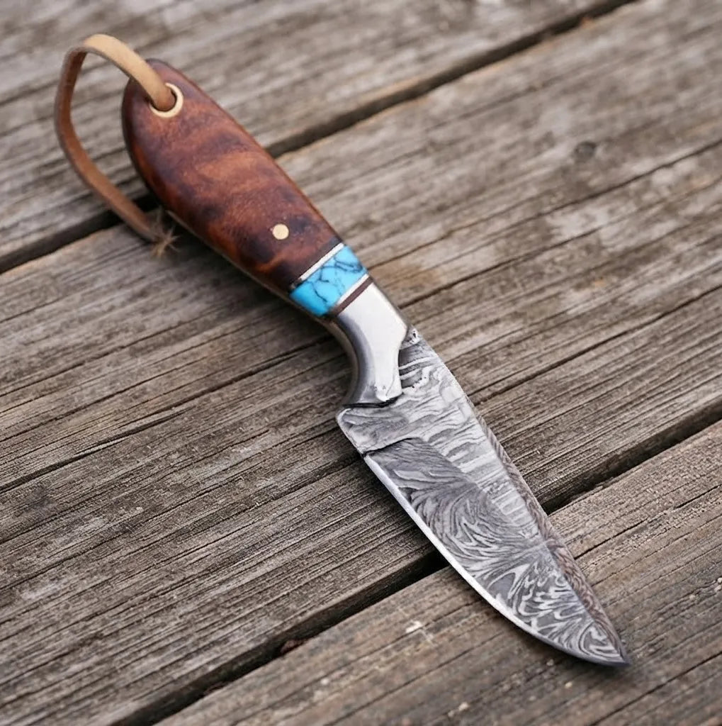 Close-up of a handmade Damascus steel cowboy hunting knife with an exquisite rosewood handle and vibrant turquoise inlay, resting on a rustic wooden surface