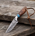 Handmade Damascus cowboy hunting knife featuring a premium rosewood handle with turquoise inlay, a fixed blade, and a leather lanyard, displayed on a rustic wooden surface