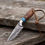 Handmade Damascus cowboy hunting knife featuring a premium rosewood handle with turquoise inlay, a fixed blade, and a leather lanyard, displayed on a rustic wooden surface