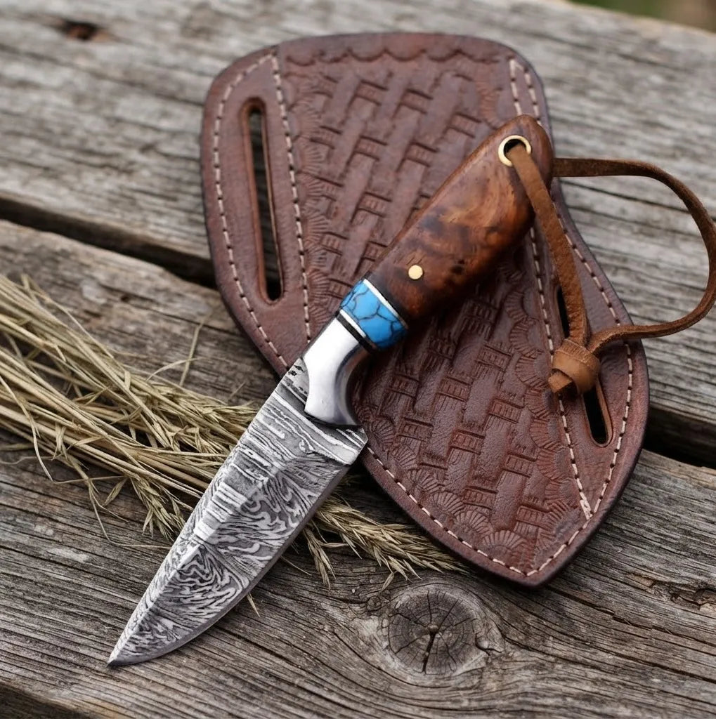 A professional handmade Damascus steel cowboy hunting knife featuring a rosewood handle with turquoise inlay, paired with a detailed tooled pancake leather sheath on a rustic wooden background.