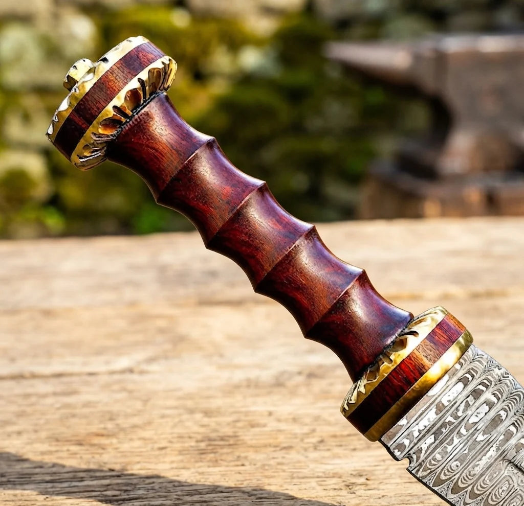 A professional macro close-up of a handmade Damascus Roman Gladius sword focusing on the contoured wooden grip, brass-accented pommel, and patterned Damascus steel blade base on a rustic wooden table