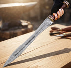 A professional action shot of a person holding a handmade 24-inch Damascus steel Roman Gladius sword, showcasing the central fuller groove, sharp tip, and wooden workbench background.