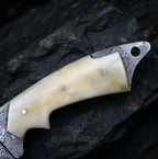 Close-up view of a premium handmade Damascus skinner knife featuring an ergonomic camel bone handle, brass pins, and full-tang steel construction