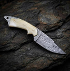 A close-up view of a handmade Damascus steel skinner knife showcasing its intricate 512-layer blade pattern and smooth camel bone handle, resting on a dark stone surface