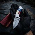 A close-up hand-held view of a handmade Damascus steel skinner knife featuring a unique American flag handle, perfect for EDC and hunting tasks.
