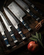 A high-quality handcrafted kitchen knife set with unique blue resin handles, displayed elegantly on a wooden board with a pomegranate and cinnamon sticks for a rustic culinary aesthetic