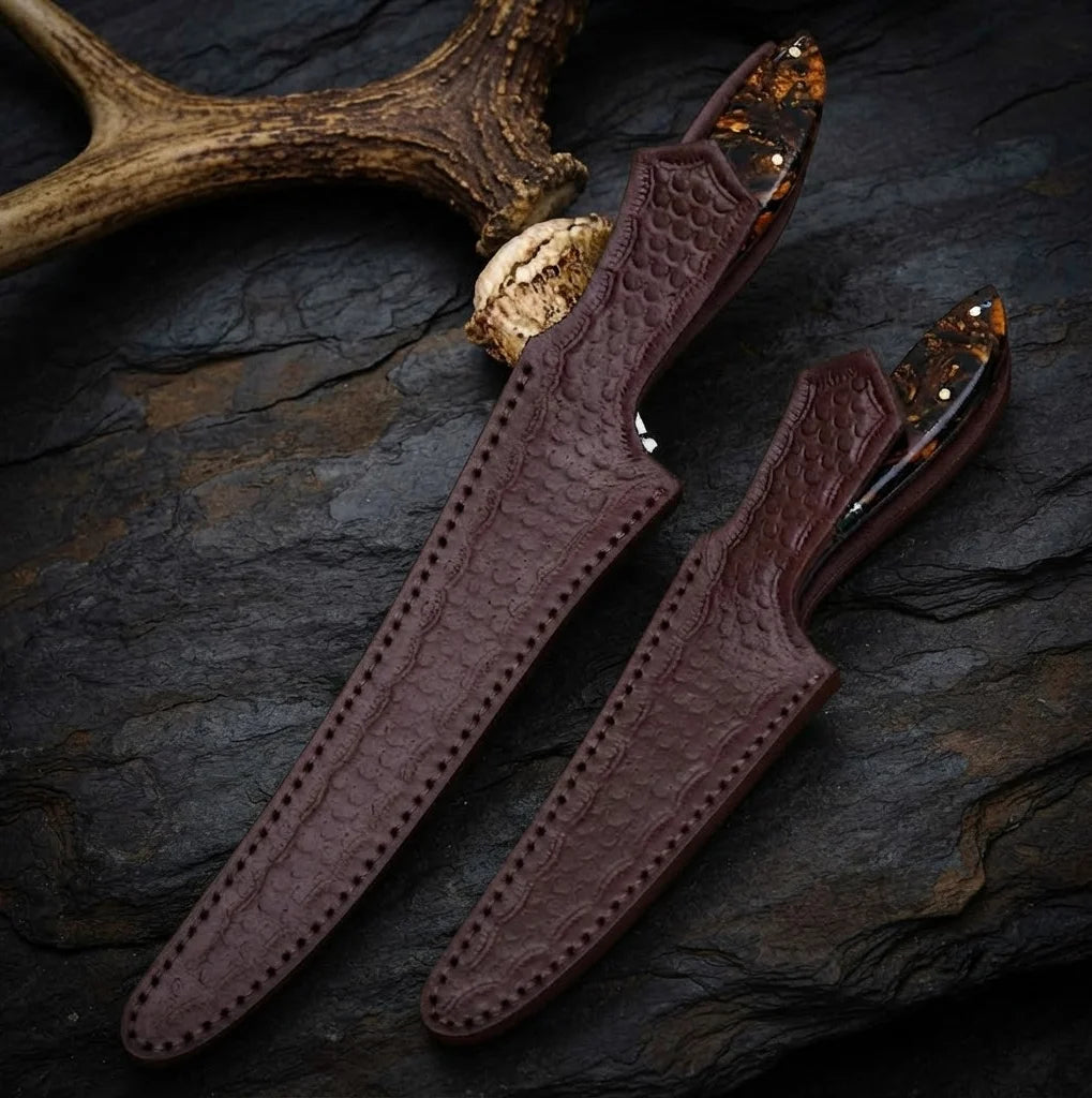 A professional handmade fillet and boning knife set safely stored in custom-tooled, embossed leather sheaths, perfect for fish and game processing.