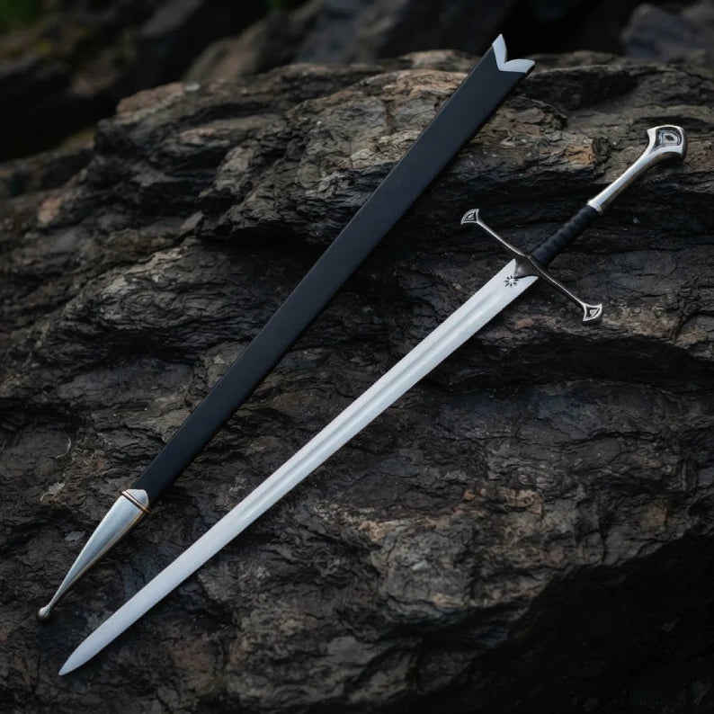 Full-length view of a handmade medieval King's sword replica and its matching scabbard, laid out on a dark, rugged stone background.