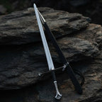 Handmade medieval King's sword replica made from carbon steel, displayed with its matching black scabbard on a rustic stone background.