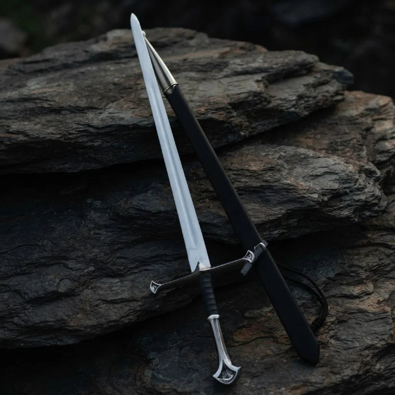 Handmade medieval King's sword replica made from carbon steel, displayed with its matching black scabbard on a rustic stone background.