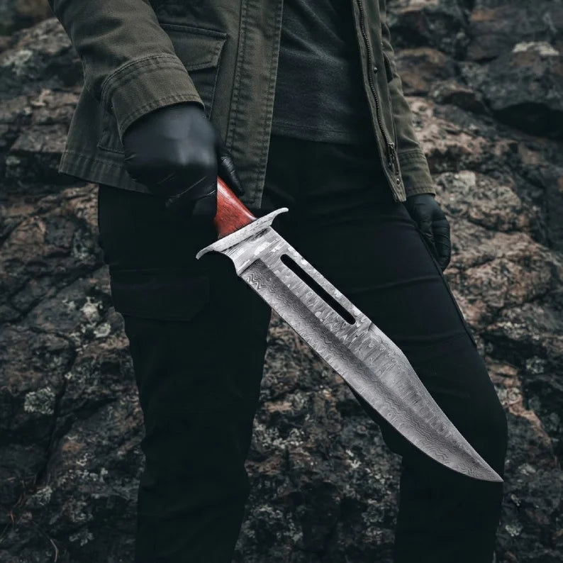 A professional handmade Rambo III style Bowie knife with a VG10 Damascus steel blade held in a gloved hand, showcasing its impressive size and tactical design