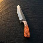 A professional studio shot of a handmade Rasp Forged D2 steel skinning knife with a turquoise marble handle and copper bolster, angled on a dark stone surface