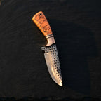 A professional studio photo of a handmade Rasp Forged D2 steel skinning knife featuring a vibrant turquoise marble handle and copper bolster on a dark stone surface