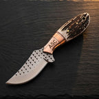 A professional top-down view of a handmade Western belt knife featuring a D2 rasp steel blade, engraved ASC copper bolster, and genuine stag horn handle on a dark stone surface