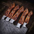 A set of luxury hand-forged Damascus steel kitchen knives featuring unique wavy blade patterns and intricate, hand-carved wooden handles, arranged with cinnamon and bay leaves