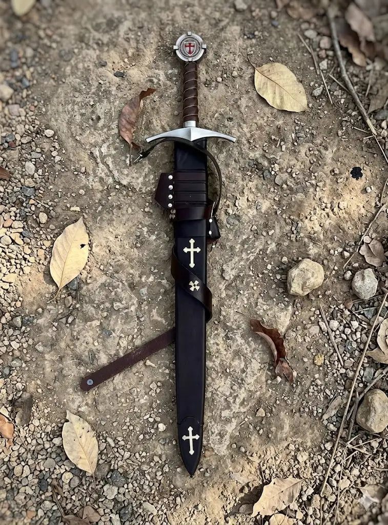 Premium handcrafted Crusader sword and scabbard set, featuring a secure leather-wrapped hilt and a heavy-duty leather protective sheath with historical cross accents, photographed in a rustic outdoor setting.