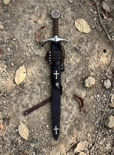 Premium handcrafted Crusader sword and scabbard set, featuring a secure leather-wrapped hilt and a heavy-duty leather protective sheath with historical cross accents, photographed in a rustic outdoor setting.