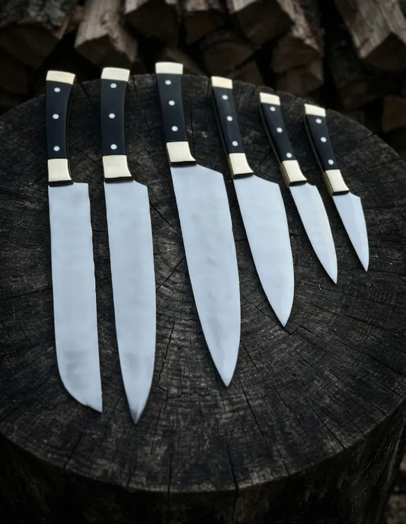 A professional 6-piece handcrafted kitchen knife set featuring classic black handles with brass bolsters, arranged on a rustic wooden log background.