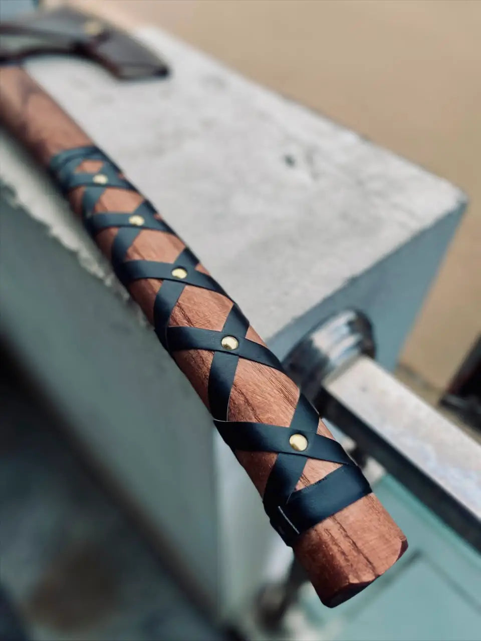 Macro view of a custom Nordic hatchet handle highlighting the premium leather wrap grip and ergonomics, showcasing artisanal craftsmanship for high-quality outdoor and tactical axes.